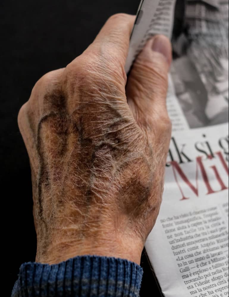An old man's hand holding newspaper